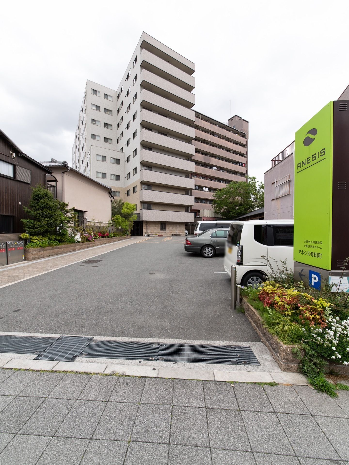 敷地内への出入口の所に花壇を設け、黄緑の看板を掲げている。看板の下に駐車場を案内する矢印マークがあり、入って右側に駐車スペースがある。