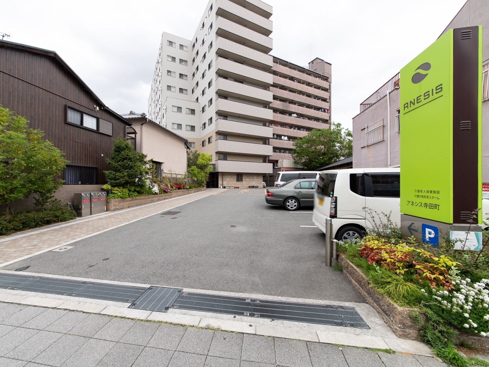 道路から入ってすぐの所に駐車スペースを設け、その奥に10階建ての建物がある。道路から目に留まる位置に看板を掲げている。
