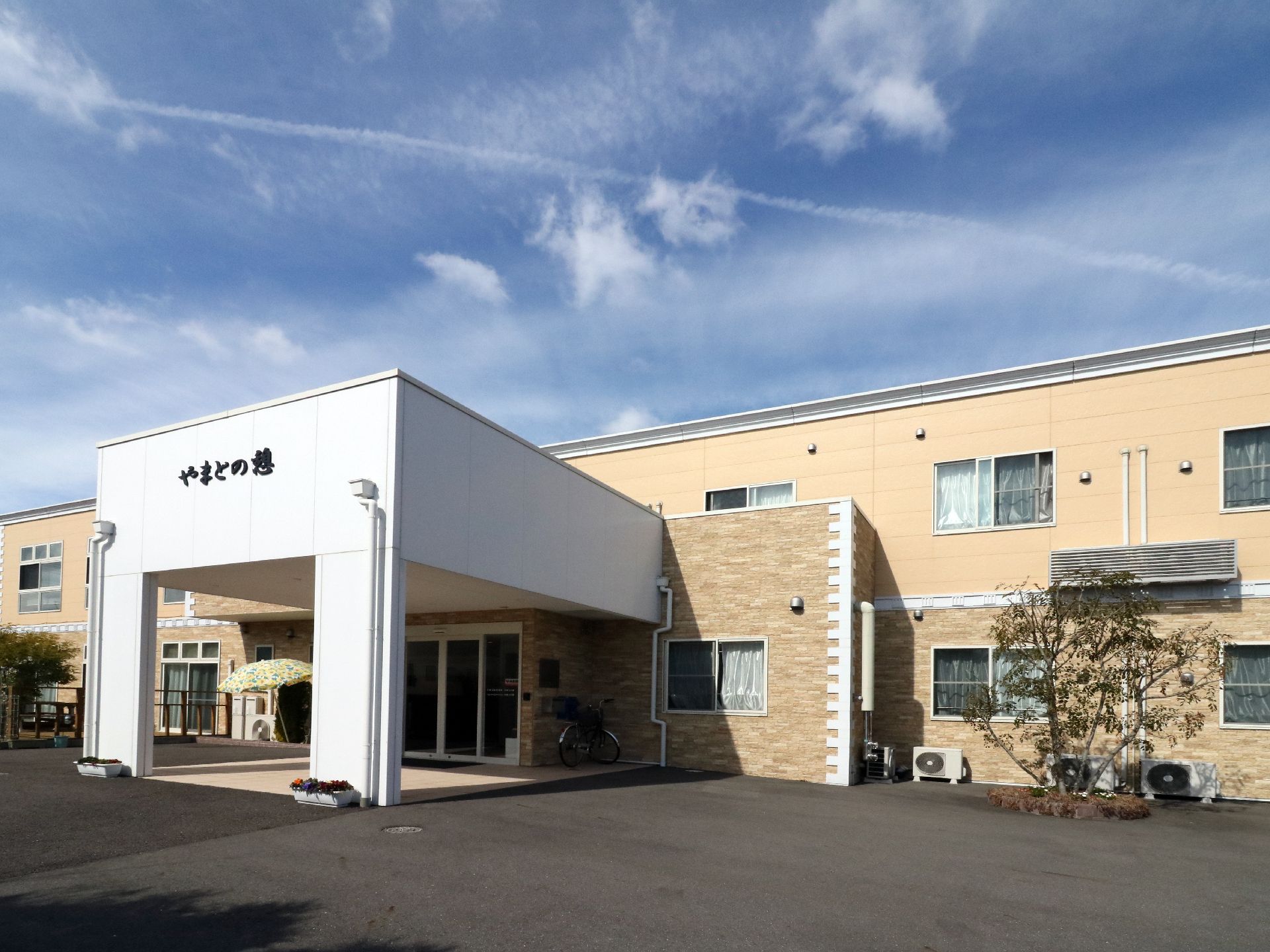 クリーム色で二色に塗り分けられた二階建ての施設。中央の入り口が大きくはりだしており、車から雨に濡れずに入館できる。