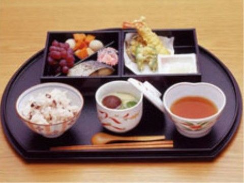 黒いおぼんに豆ごはんや茶わん蒸しなどが盛りつけされた食事