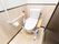 居室内のトイレは壁が木目調になっている。固定式の手すりが取りつけられている。折り畳み式の手すりが追加で置かれている。