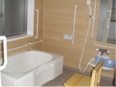一人用の浴槽。シャワーの前には椅子が置いてある。壁にはたくさんの手すりが取り付けてあり、大きな窓がある。