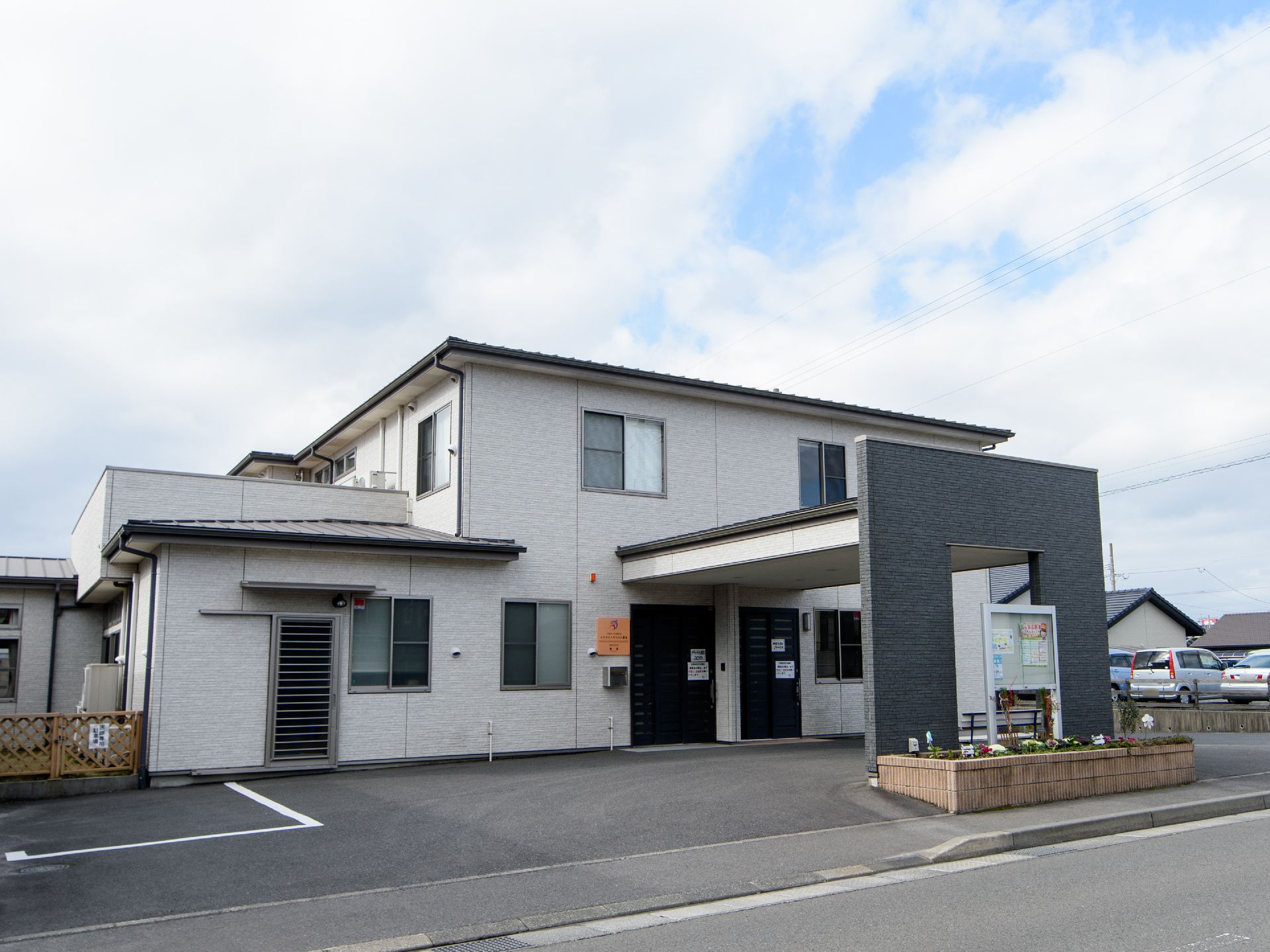車道に面した場所に、白と紺のシンプルなデザインの住宅が建っている。玄関前は車が寄せられるスペースがあり、屋根がついている。