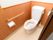 木の引き戸を開けると洋式のトイレがある。壁には手すりが設置されていて、便座には花柄のカバーが掛かっている。