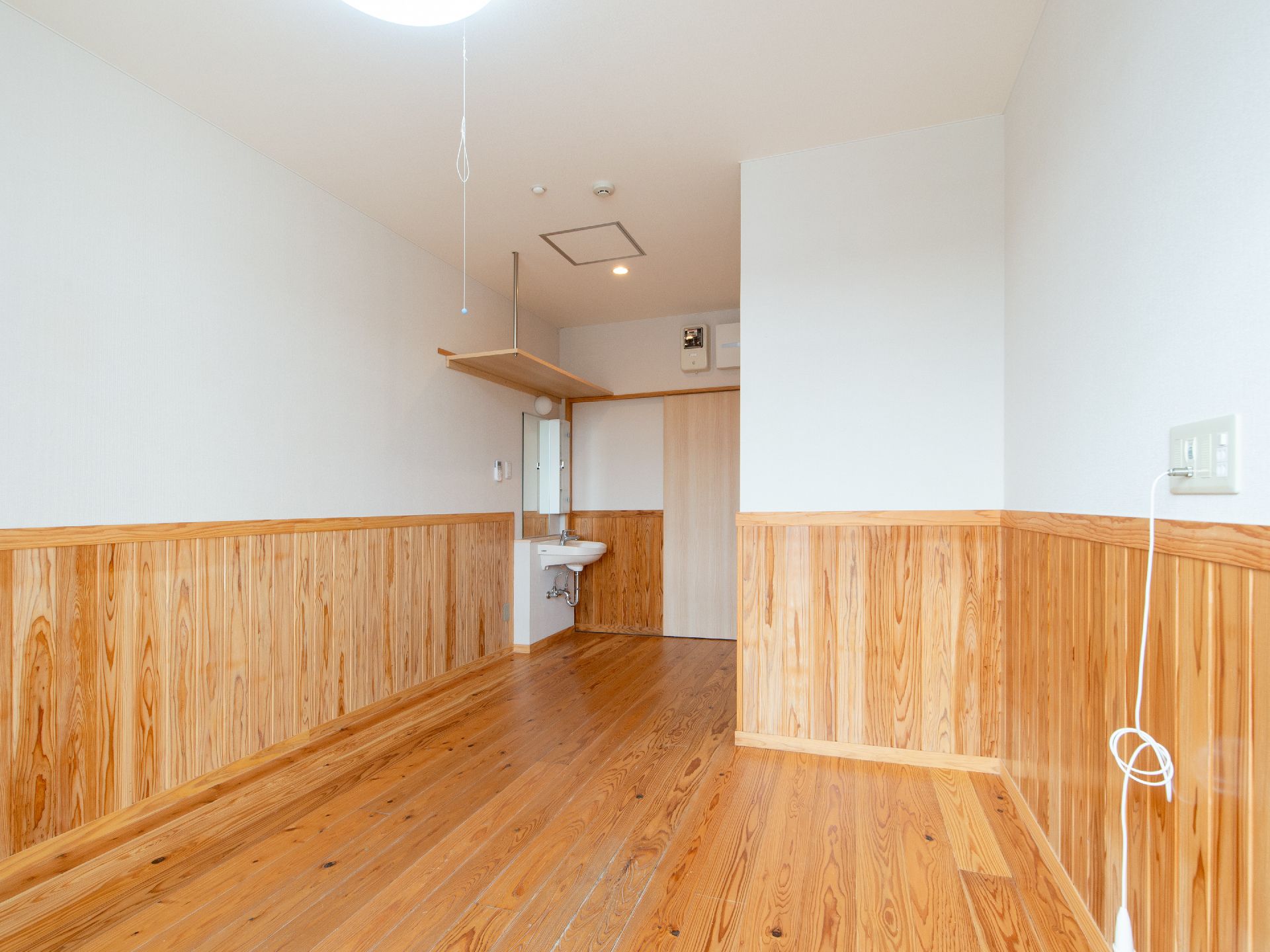 広い通路のつきあたりには緑の誘導灯が光っている。通路の途中に椅子が2脚置いてあり、壁には手すりが伸びている。