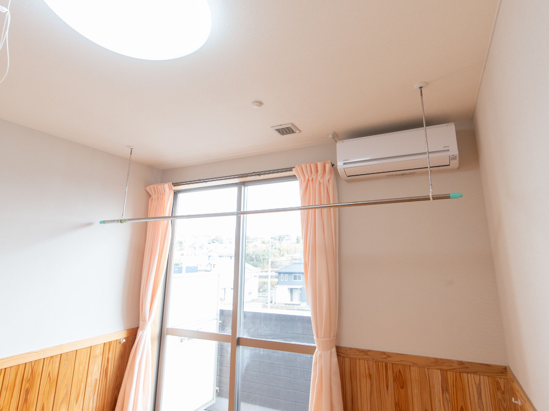 大きなはき出し窓に向かいの緑の屋根の家や景色が写っている。天井には大きな丸い照明があり、換気口も設置されている。