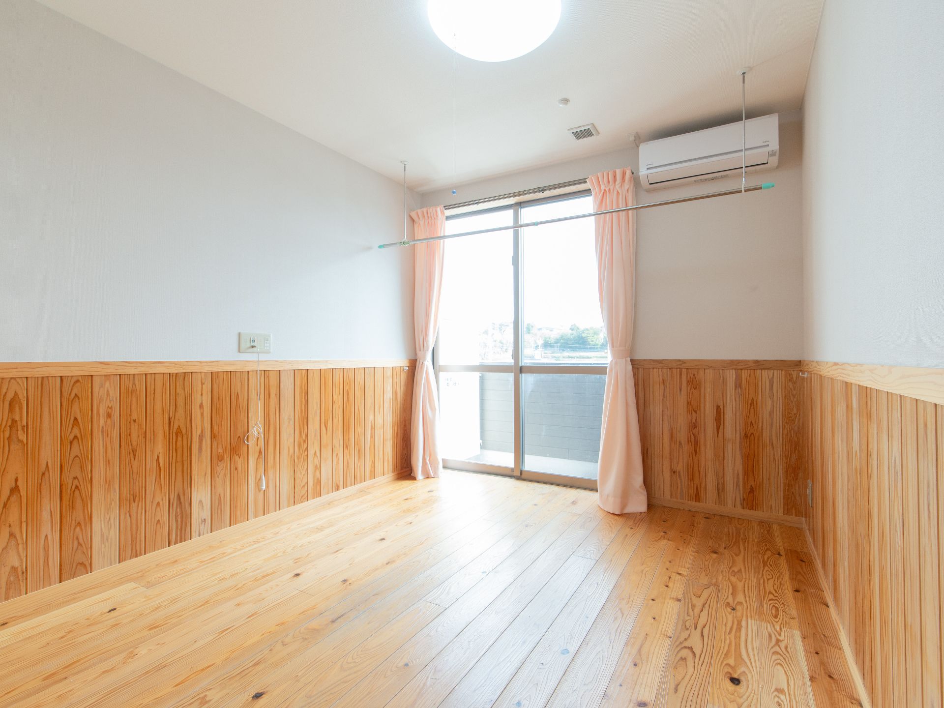 床と腰の高さまで木板があしらわれた、白い壁の広く明るい部屋である。太陽の光が降り注ぐ地窓には、オレンジ色のカーテンが束ねられている。