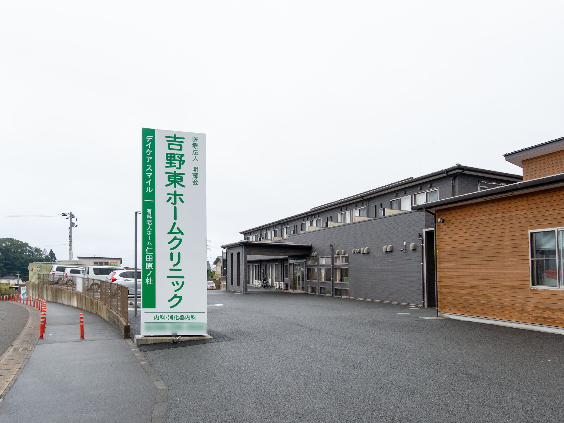 施設の敷地内に隣接してクリニックが建っている。散歩道と敷地の庭の間に、クリニックの白地に緑文字の大きな看板が立っている