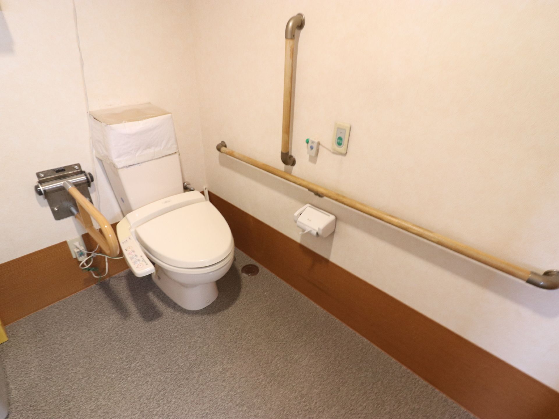 広いスペースが確保されたトイレである。手すりが複数設置されており、呼び出しボダンも備え付けられている。