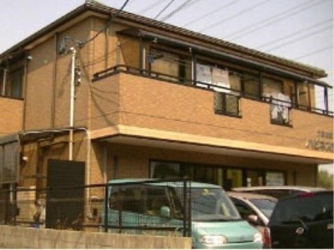 建物前に車が停められ、２階のベランダに洗濯物が干されている施設外観