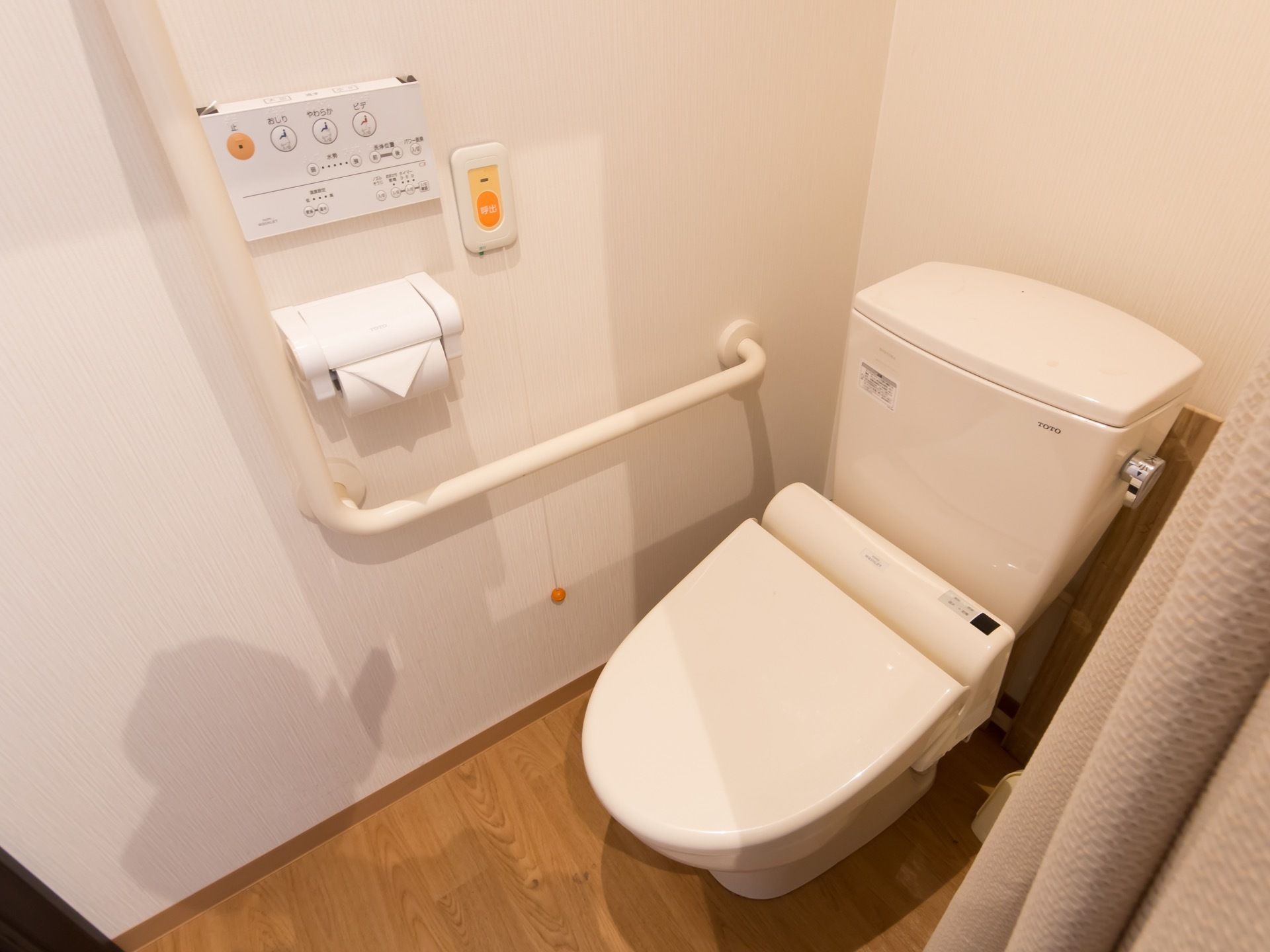 洋式トイレの横の壁に、ペーパーホルダーと温水洗浄便座のリモコン、手すり、ナースコールが設置されている。