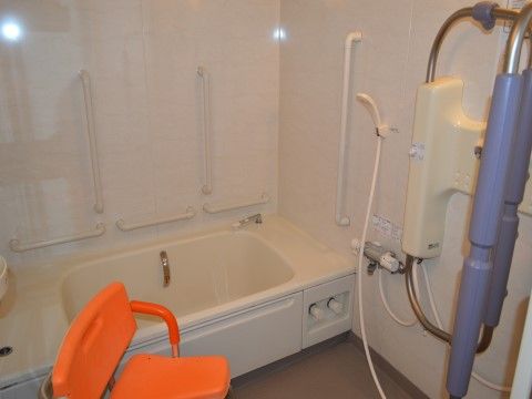 浴槽の周りに手すりがたくさん備え付けられた浴室となっている。シャワーの前にはシャワーベンチが置かれている。