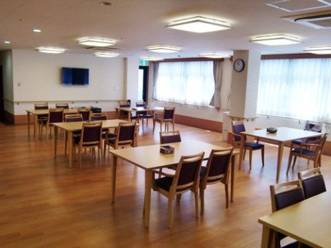 共有スペースは壁一面が窓になっていてとても明るい。４人掛けのテーブルセットが並び、壁に液晶テレビが掛けられている。