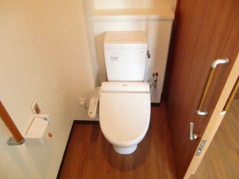 居室のトイレは引き戸になっている。便座横のスイッチで操作する温水洗浄便座が用意されている。壁には非常ボタンと手すりが設置されている。
