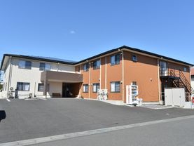 朱色と白の外壁がおしゃれな外観。施設敷地内には大きな駐車場を完備している。車いすでの利用も楽に行える整備された路面。
