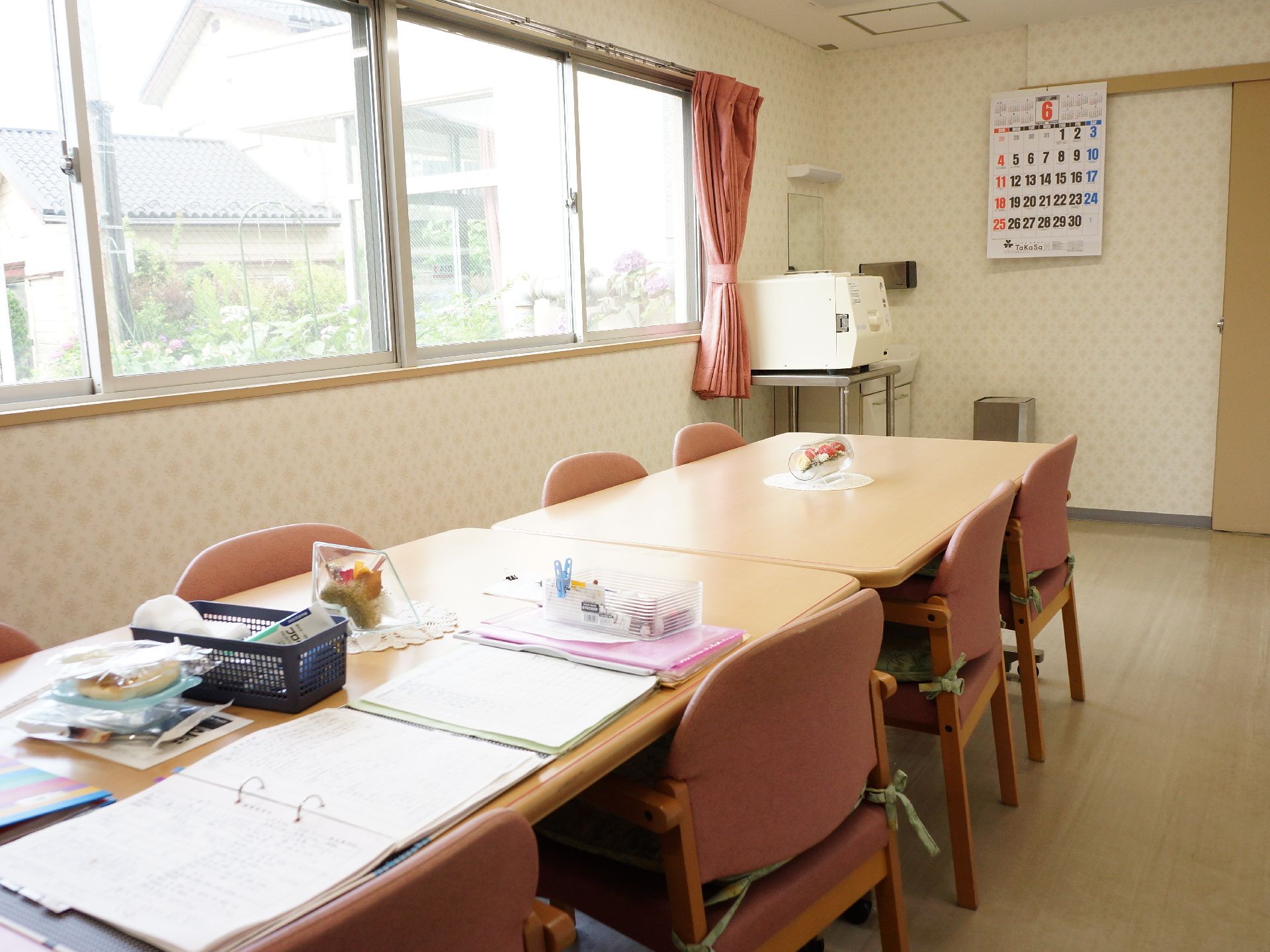 こじんまりとしたスタッフルーム。窓からは玄関や駐車場が良く見える。壁にはカレンダーがあり、洗面台等も設置されている。