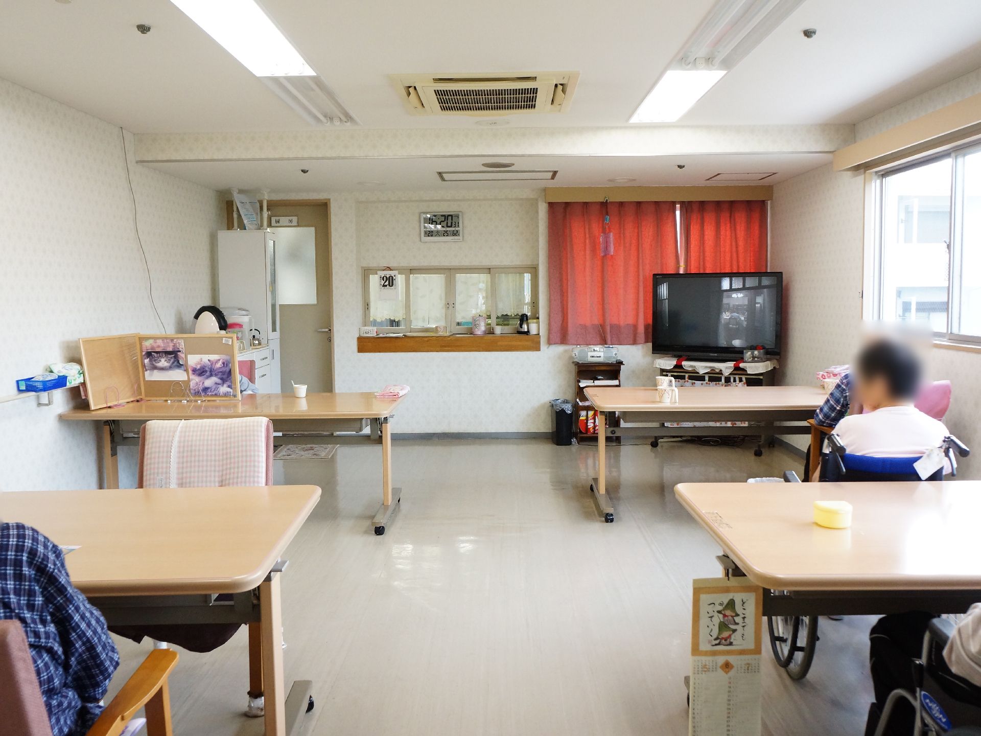 長机が4つ並べられた食堂には、1台のテレビが設置されている。左奥には、収納棚と机の上にコーヒーメーカーが並べられている。