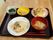 黒いトレーの上に箸と食事が並べられている。メニューは味付きのご飯にみそ汁、かき揚げと小皿の副菜が２品である。