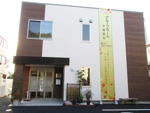 白と焦げ茶を基調としたモダンな外観の施設。建物には玄関ポーチが設けられており、外壁には施設名を書いた懸垂幕が据えられている。