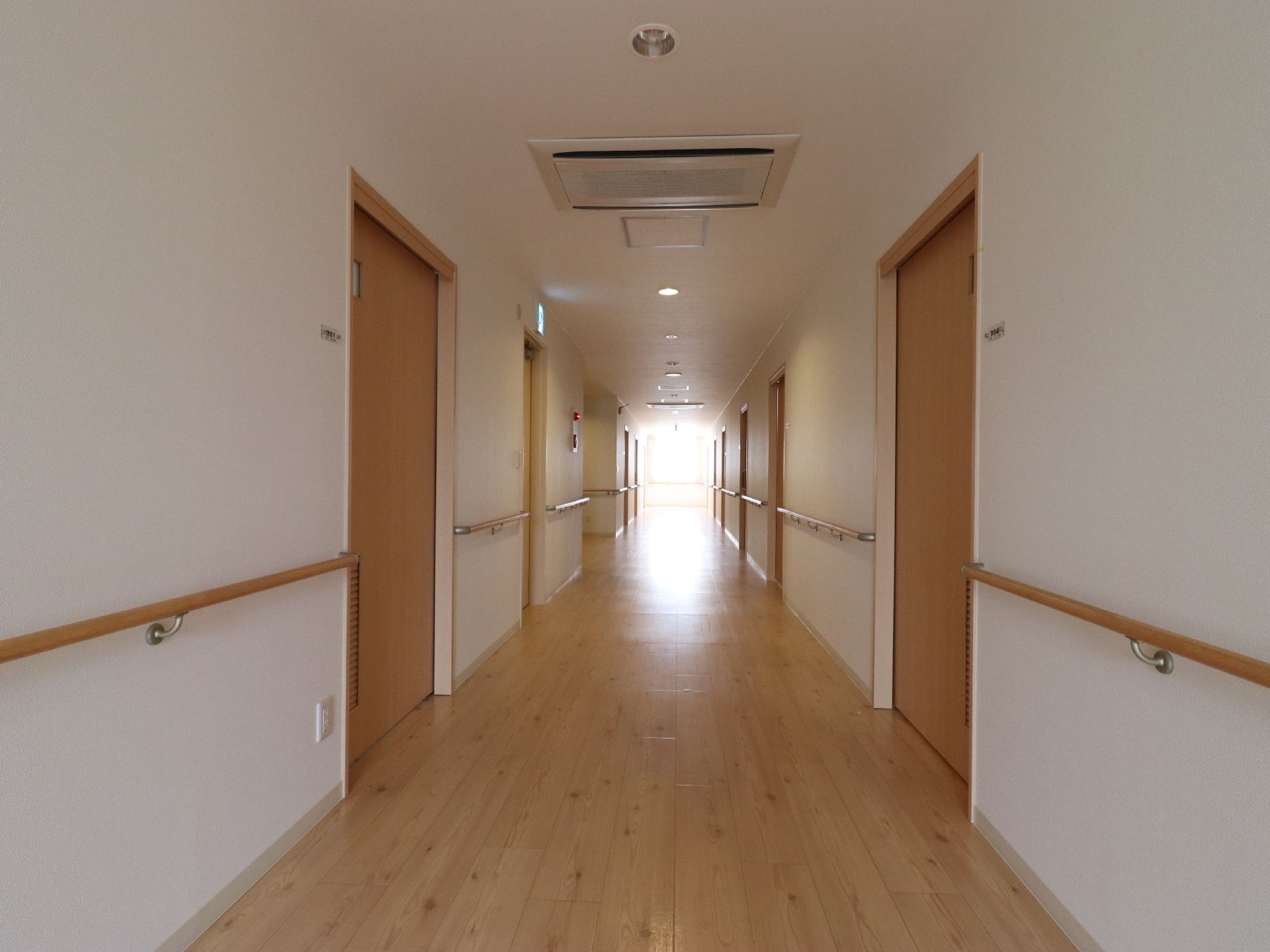 白い壁の廊下は、幅にゆとりがあり広々としている。木目の床と扉になっていて、落ち着いた雰囲気になっている。