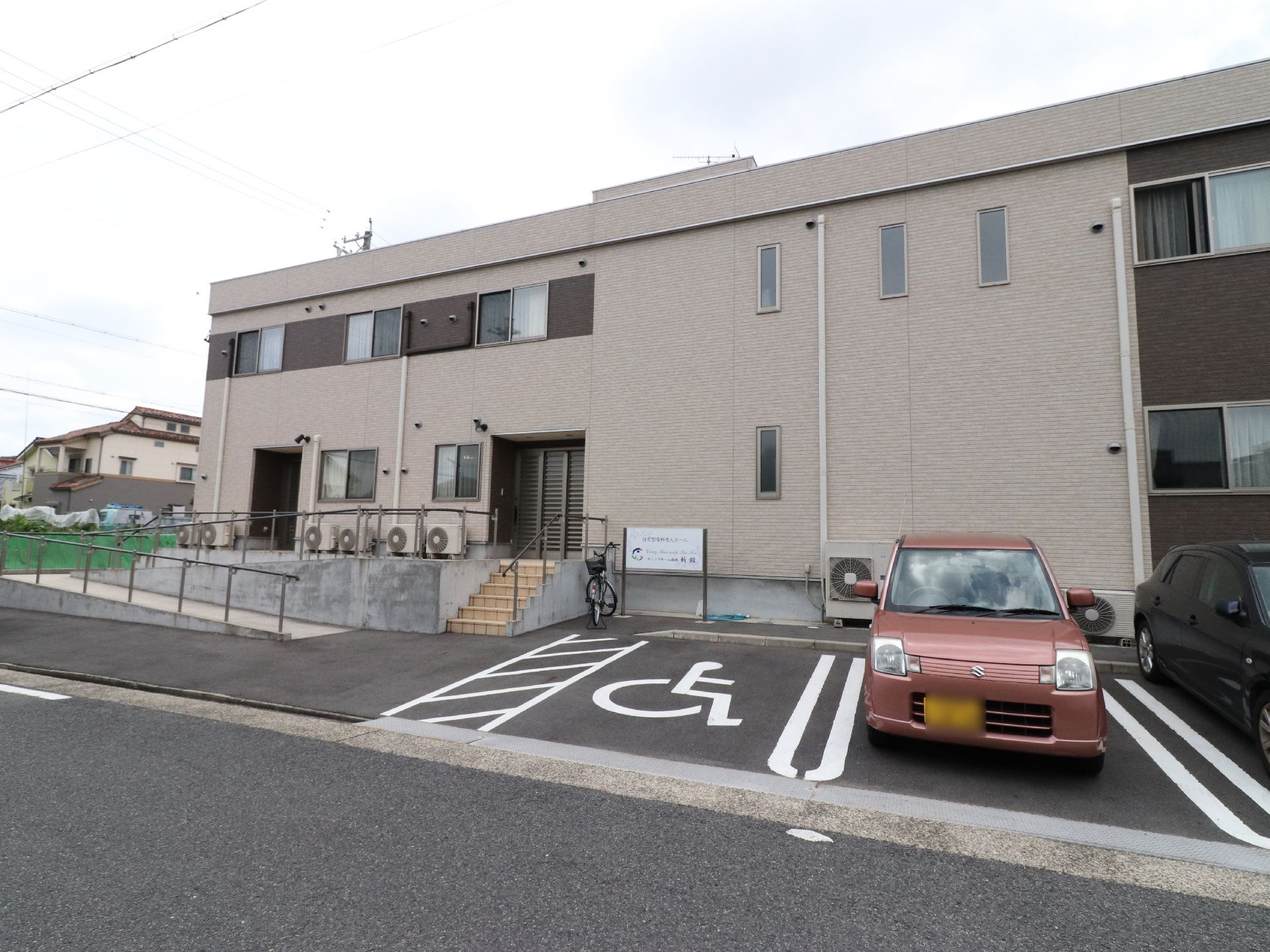 ベージュとブラウンの外壁で落ち着いた雰囲気になっている。玄関までは階段があるが、車いすの方も安心のスロープもあり安全になっている。
