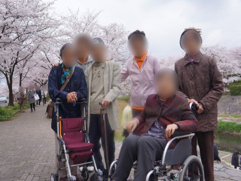 桜が満開の川沿いの遊歩道でカメラの方を見ている入居者様