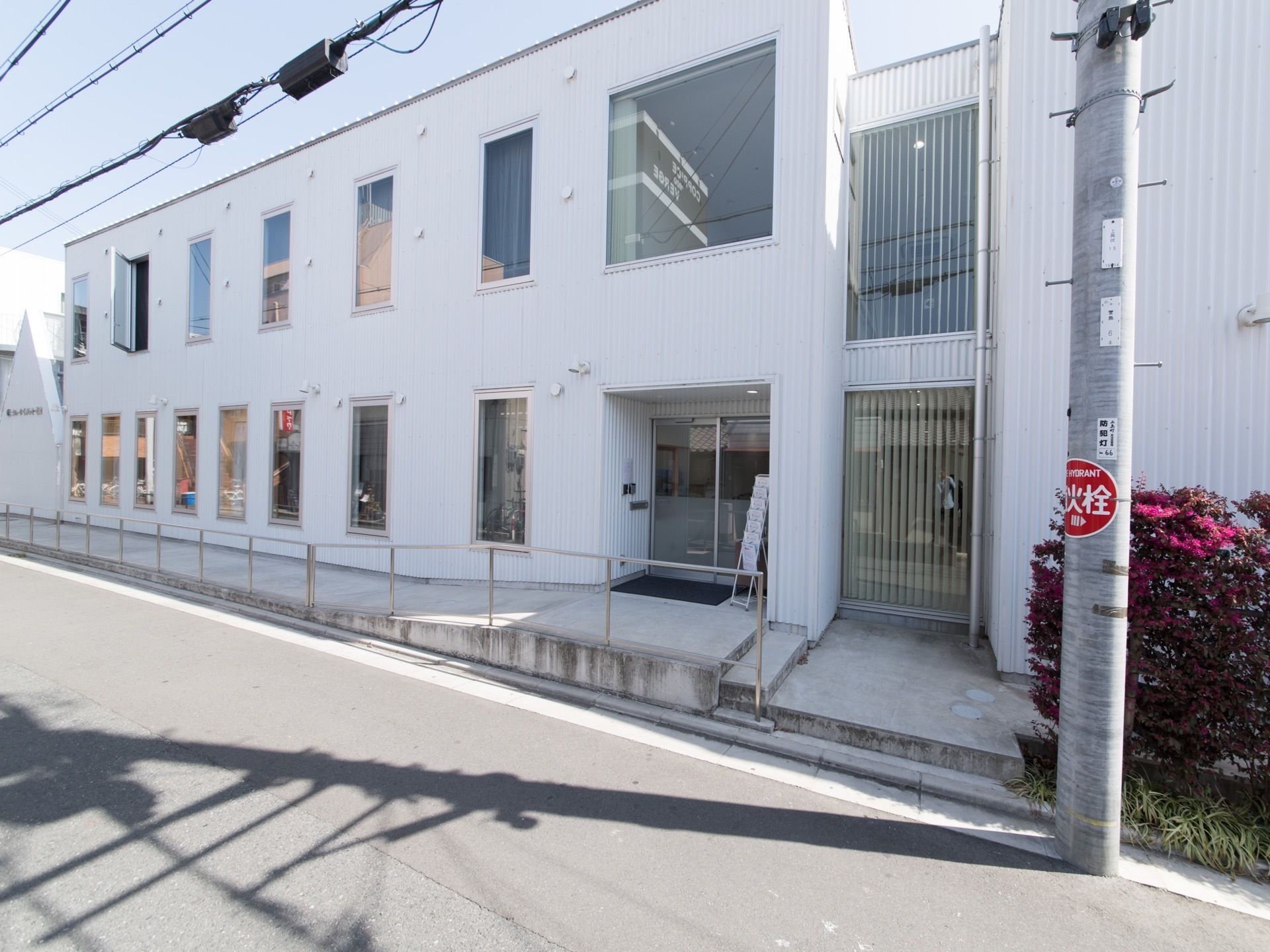 施設の建物は二階建てで、外壁の色は白で統一している。玄関はガラス張りで、入り口前にパンフレットを置いている。