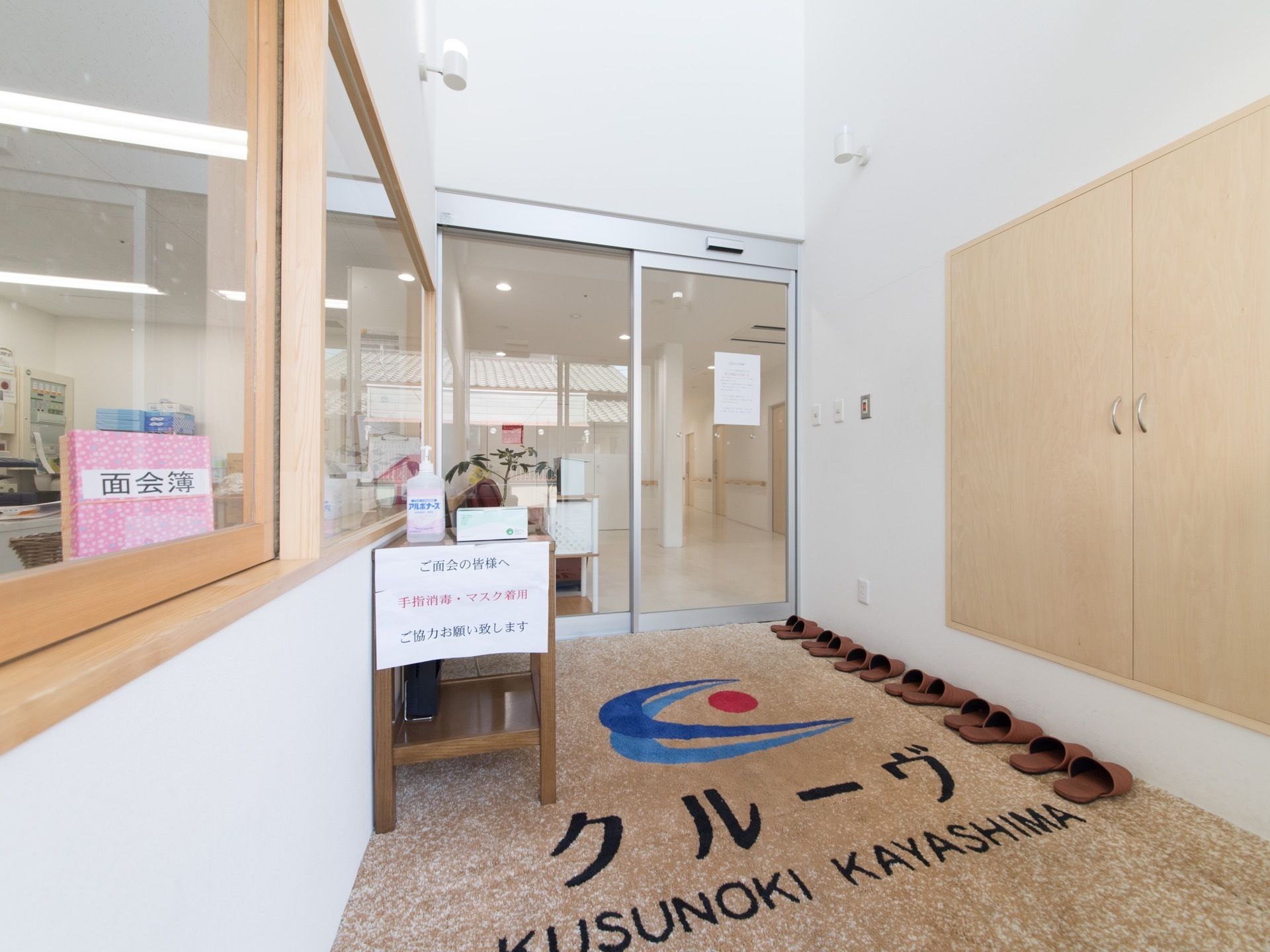 施設の玄関内部の床はフラットなカーペット敷きである。壁には受付用の窓を設け、前面には消毒用アルコールを用意している。
