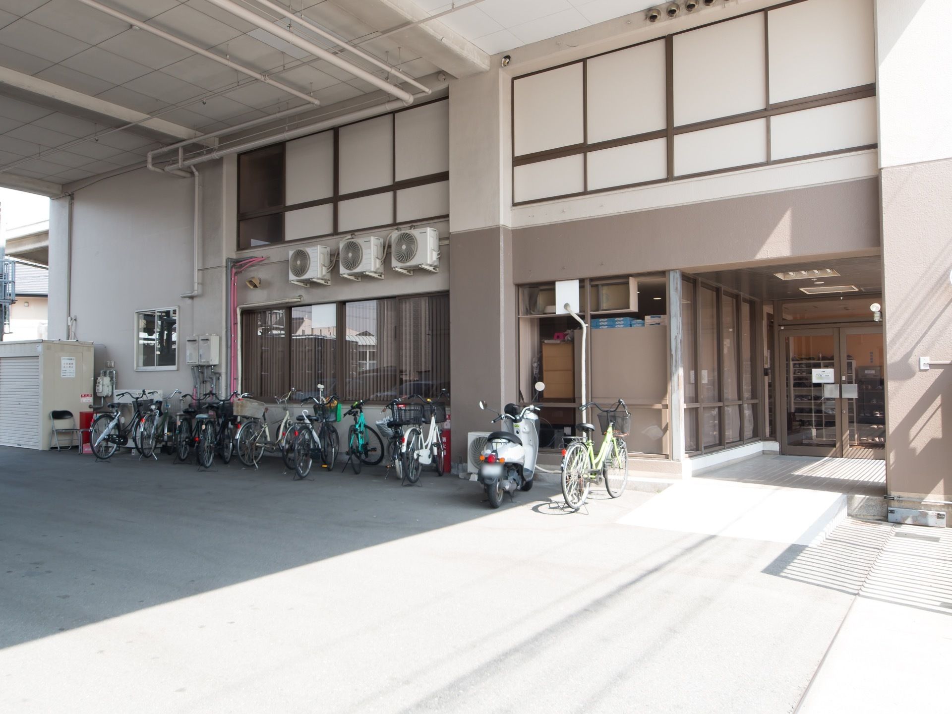 玄関前は施設の上層階が屋根になっている。そのスペースにはたくさんの自転車や原付バイクが停められている。