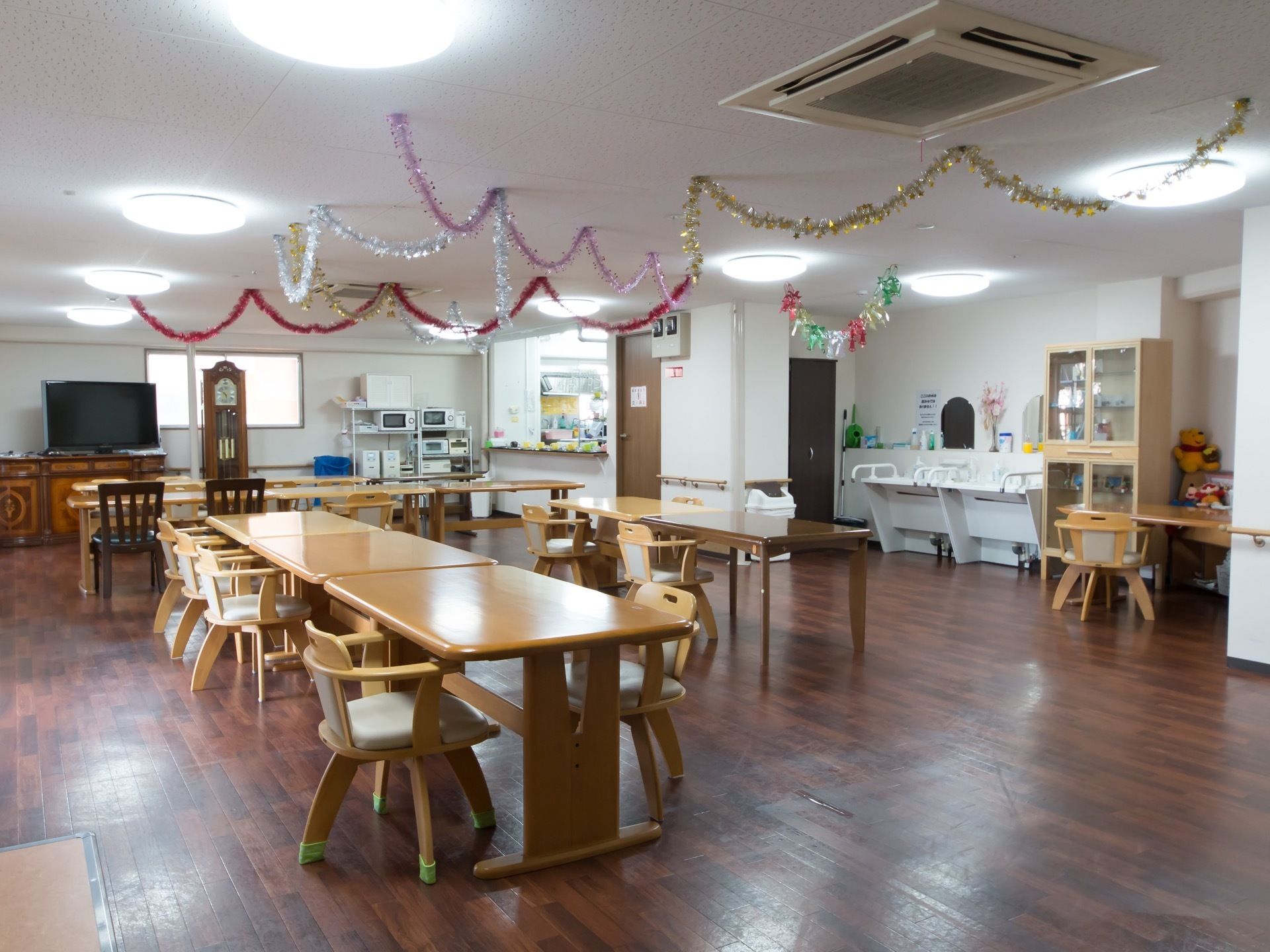 右奥に洗面台が２か所に設置され、その横に食器棚がある。左奥の壁際に大型液晶テレビと柱時計が置かれている。