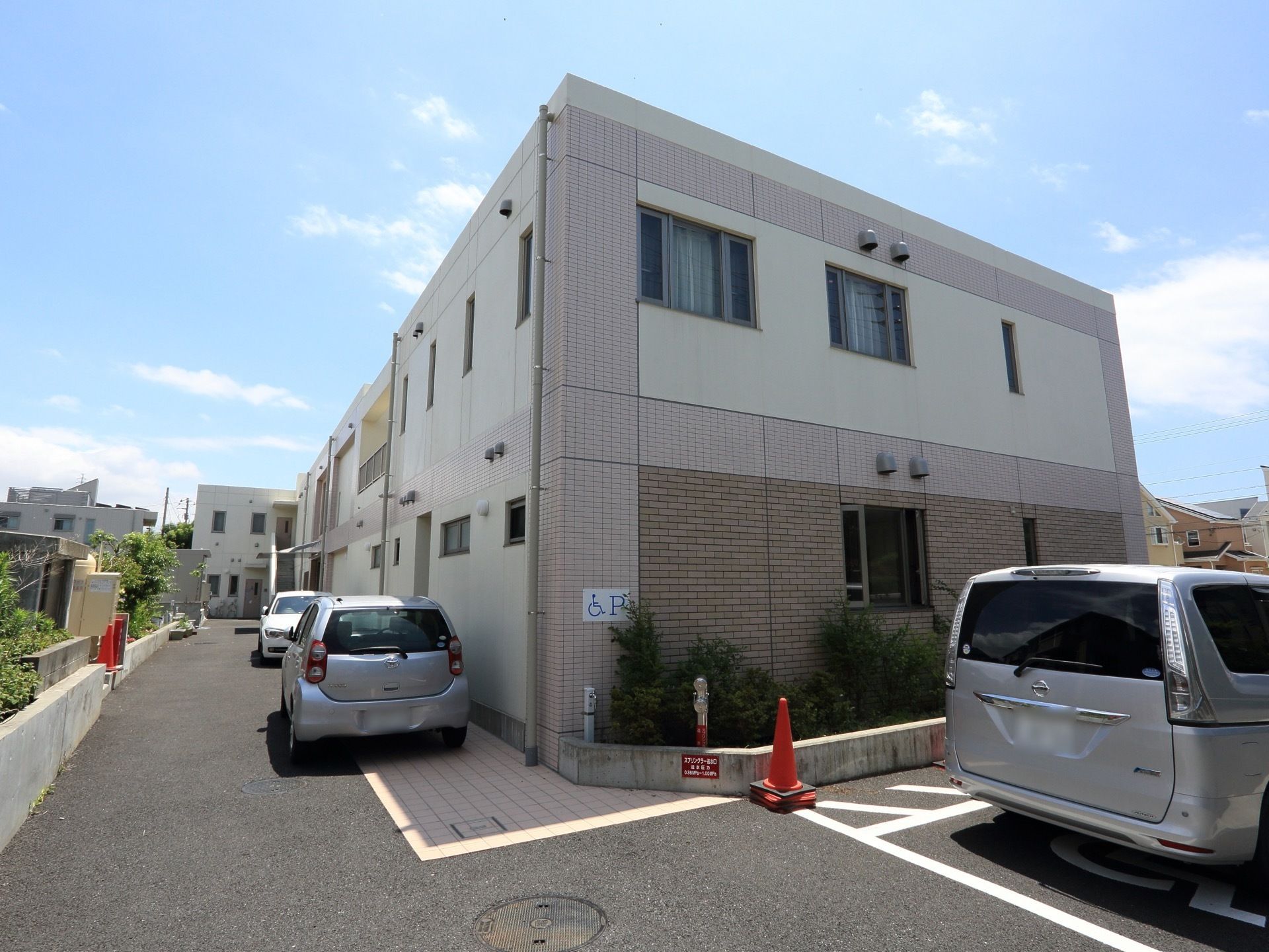 外装色がグレー基調の2階建てとなっている。その周囲は完全舗装の駐車場を完備し、閑静な住宅街の中にある。