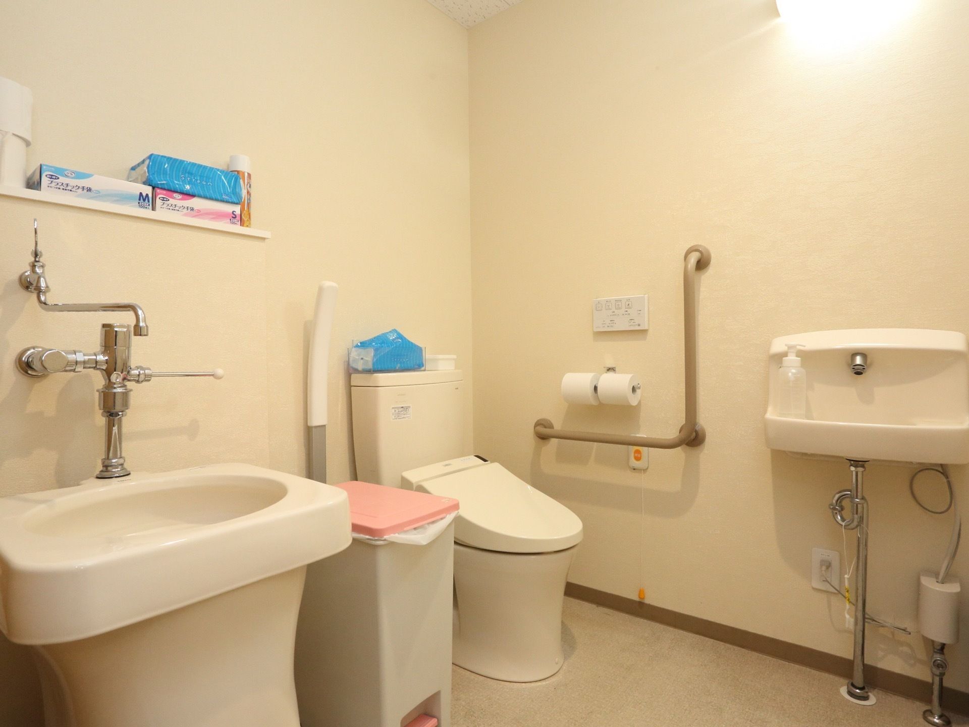 内装色がアイボリー基調の流しが直近にあるトイレである。清掃が行き届いており、数種類の備品が在庫管理されている。