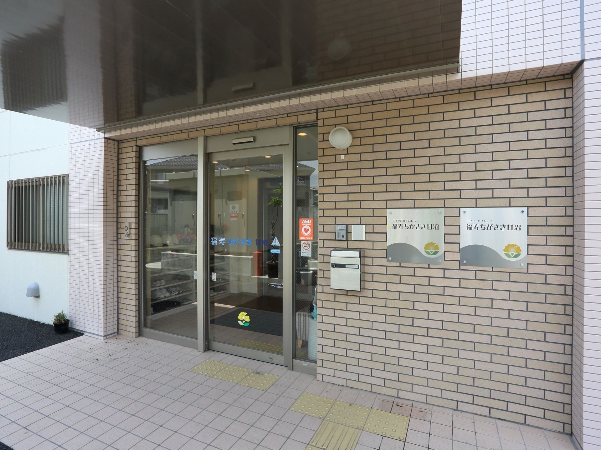 レンガ調の壁に自動ドアの付いた施設の玄関。入口には屋根が設けられている。