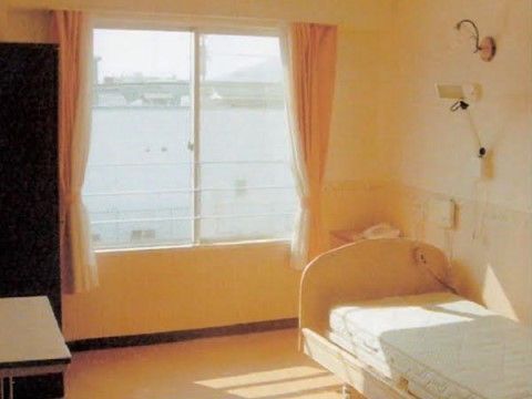 大きな窓から日差しがたっぷり入る。電動の低床型ベッド脇には、非常用ブザーがある。電話台とテーブル、クローゼットが置かれている。