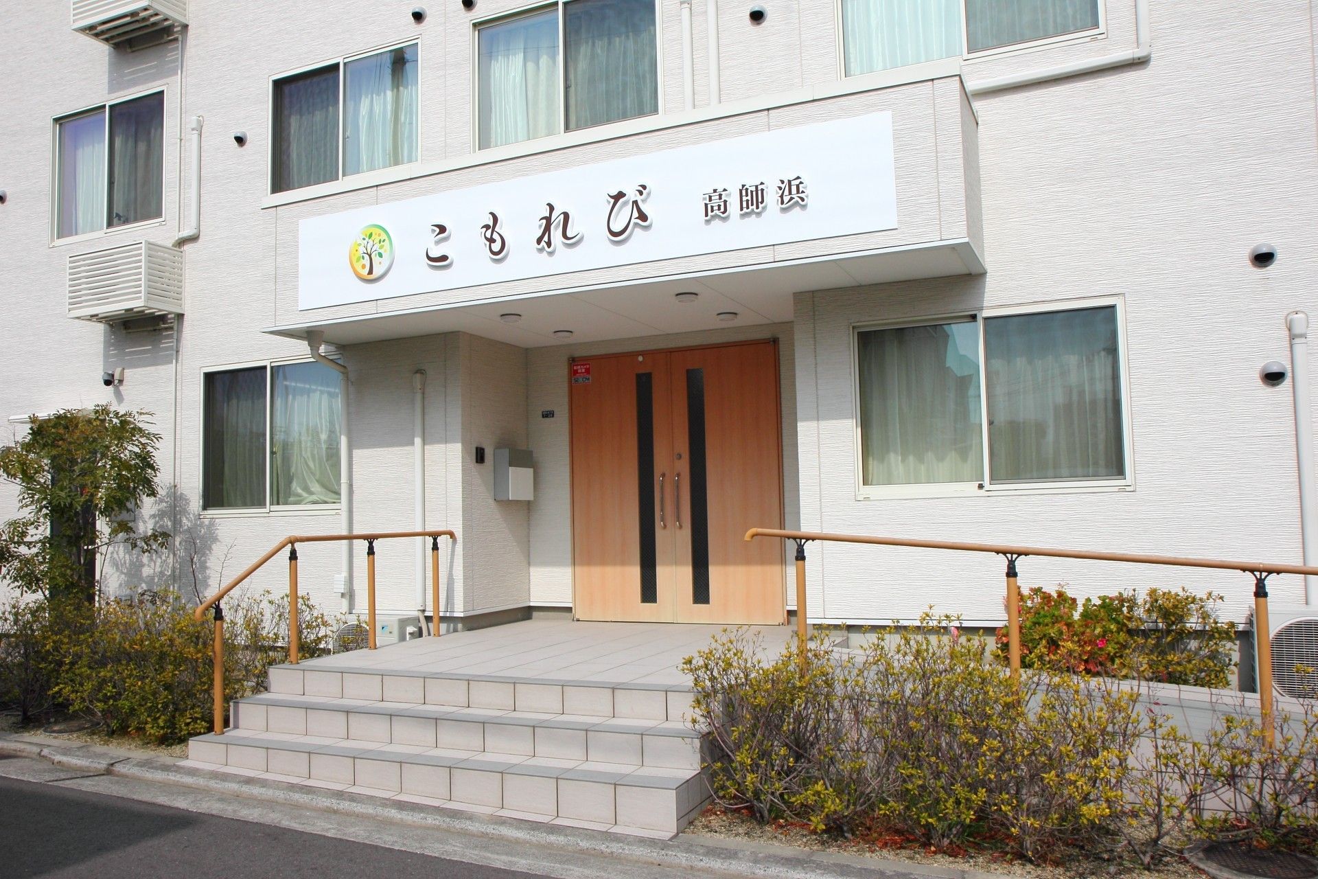 木造３階建の白い建物である。玄関のひさし部分に大きく施設の名前が入っている。手すりの付いた階段とバリアフリーのスロープが玄関に続く。