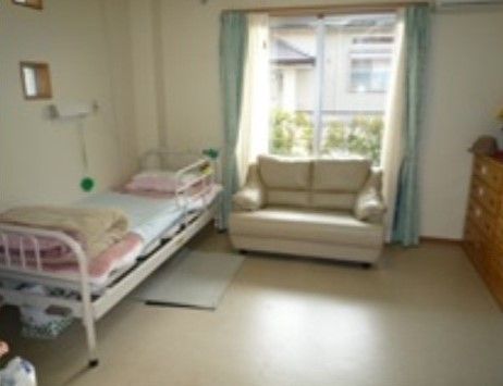 白を基調とした清潔感のある色合いの居室になっている。窓際にソファが置かれ、壁際にベッドが用意されている。