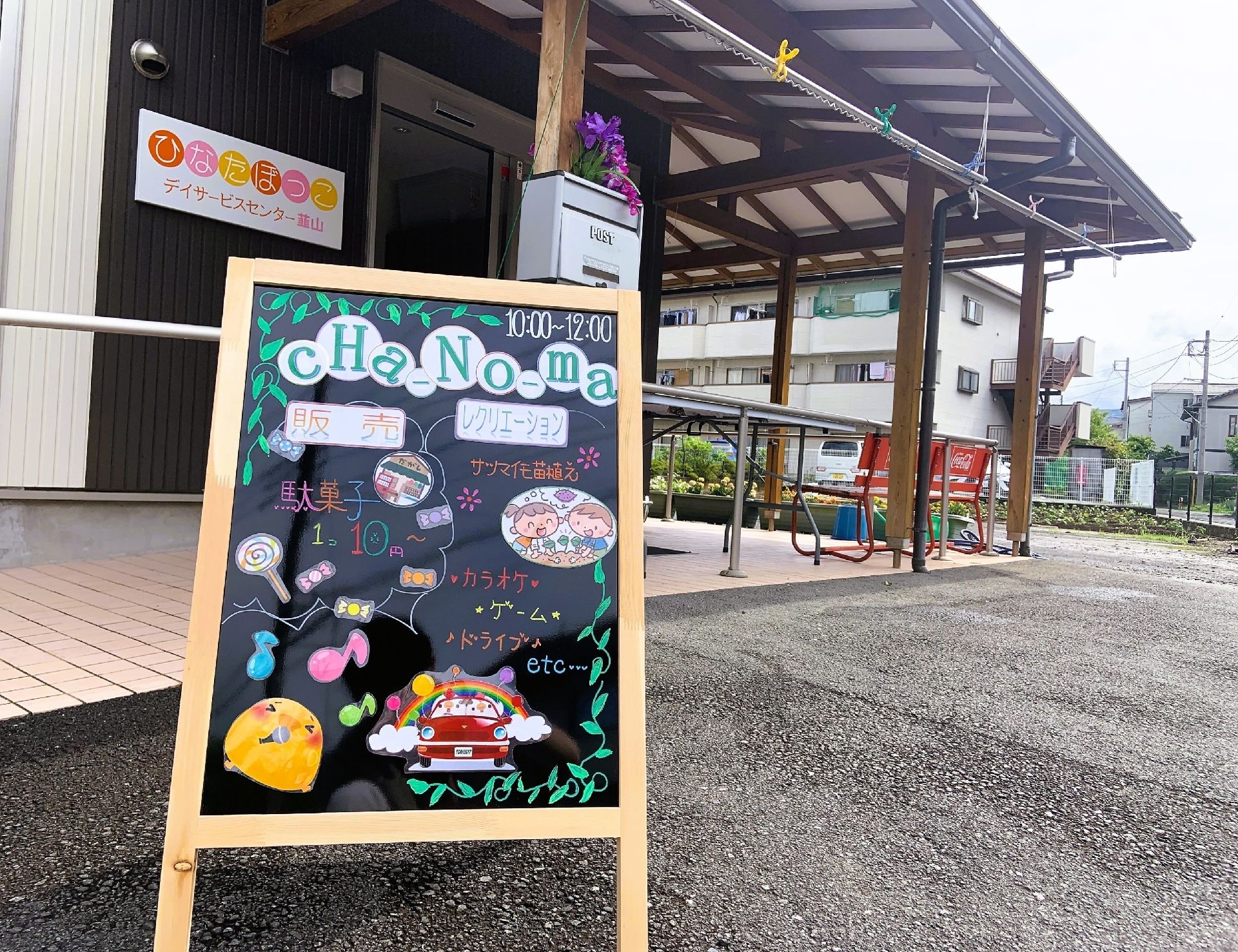 共有スペースに入居者様皆さまが集まり、女性スタッフの話を聞いている。テレビやホワイトボードが設置されている。トイレが２ヵ所完備されている。