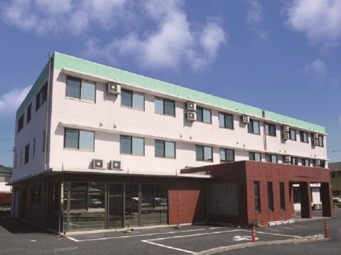 施設は白色を基調とした３階建ての建物であり、規則正しく窓が配置されている。また、入口近くには自動販売機が設置されている。