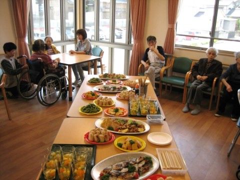 大皿料理がたくさん乗ったテーブルの周りに集まっている入居者様