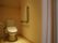 奥行きのあるトイレの入り口はカーテンが掛けられ、床はフローリングである。壁に茶色い手すりが設置されている。