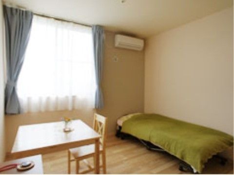 フローリングの床に若草色のベッドカバーが掛けられたベッドが置いてある。腰高窓に水色のカーテンとレースカーテンを設置している。