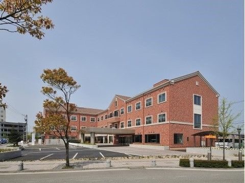 青空の下にレンガ造りの三階建て施設、その前に駐車場がある風景