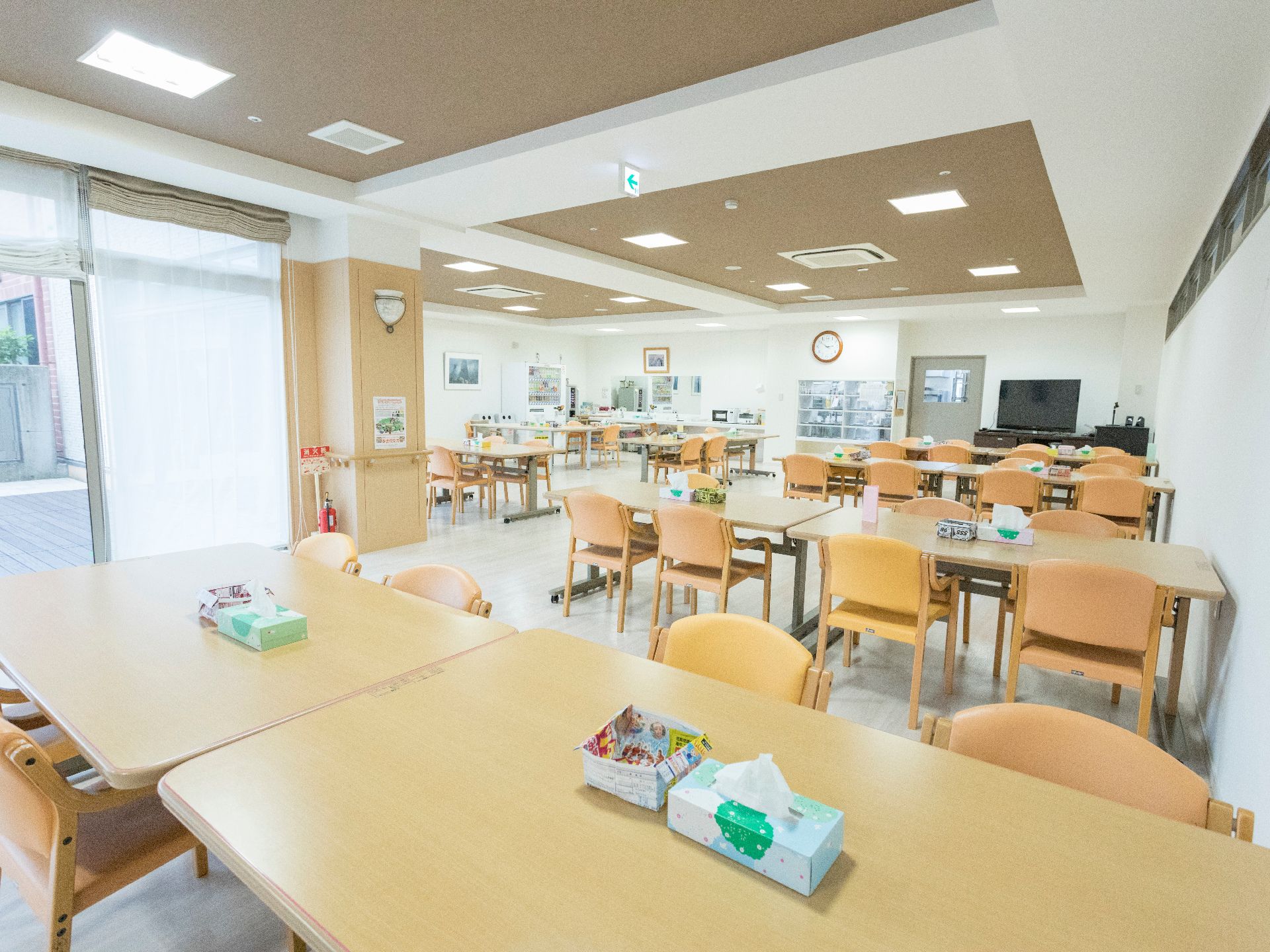 テーブルと椅子は、1つのテーブルに対して4脚の椅子がある。テーブルの上にはティシュが置かれている。周囲の壁には絵が飾られている。