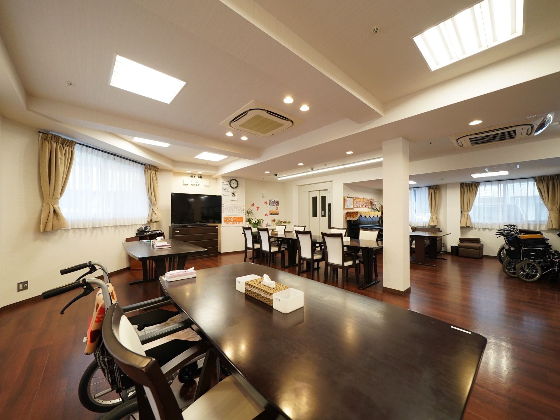 大きな部屋にダイニングテーブルと椅子のセットが数組置かれている。中央の壁際には大型テレビが設置されている。
