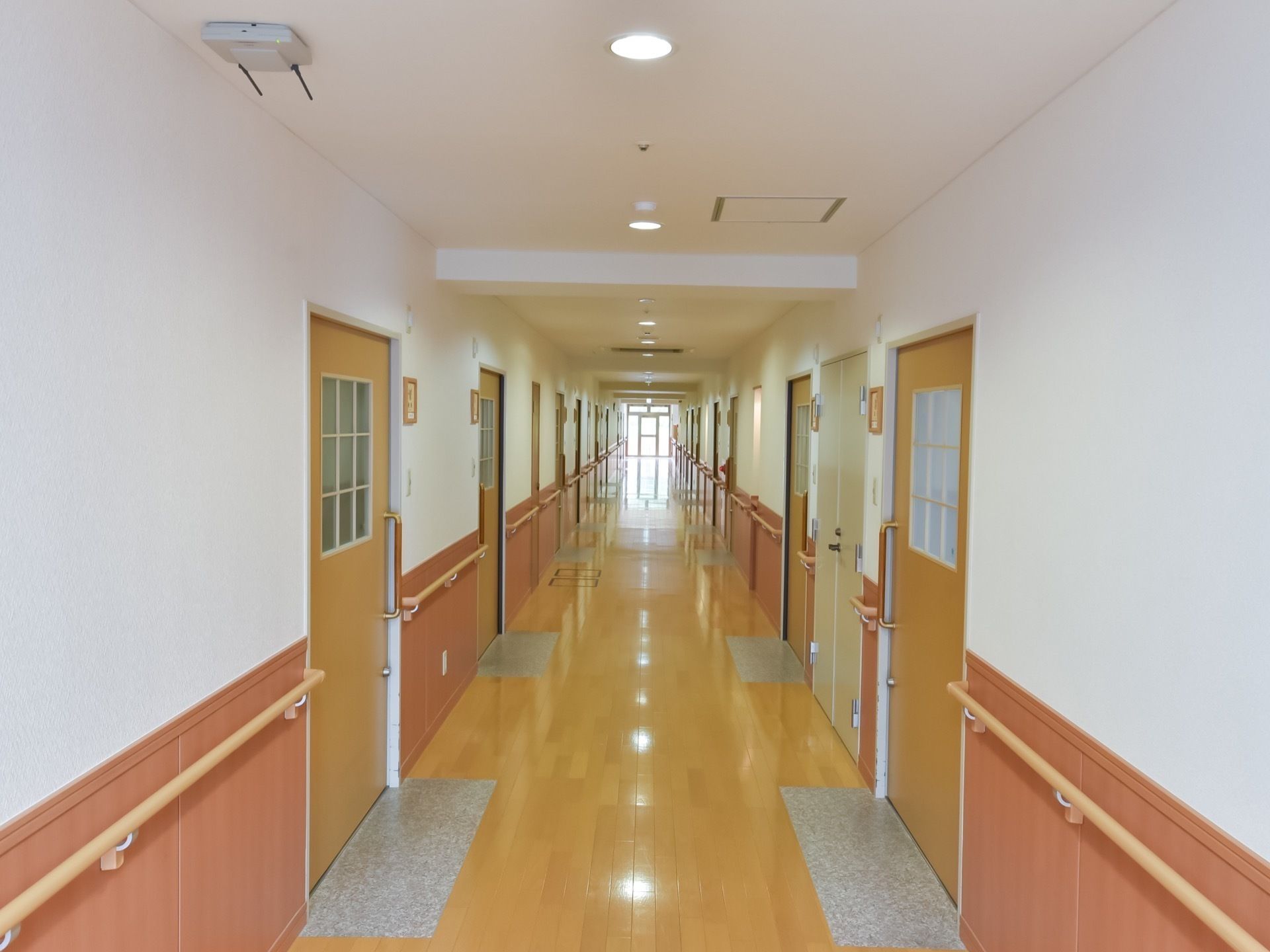 明るく真っ直ぐな廊下は、幅が広くとられている。居室のドアが左右に並んでおり、手すりが壁に取り付けられている。