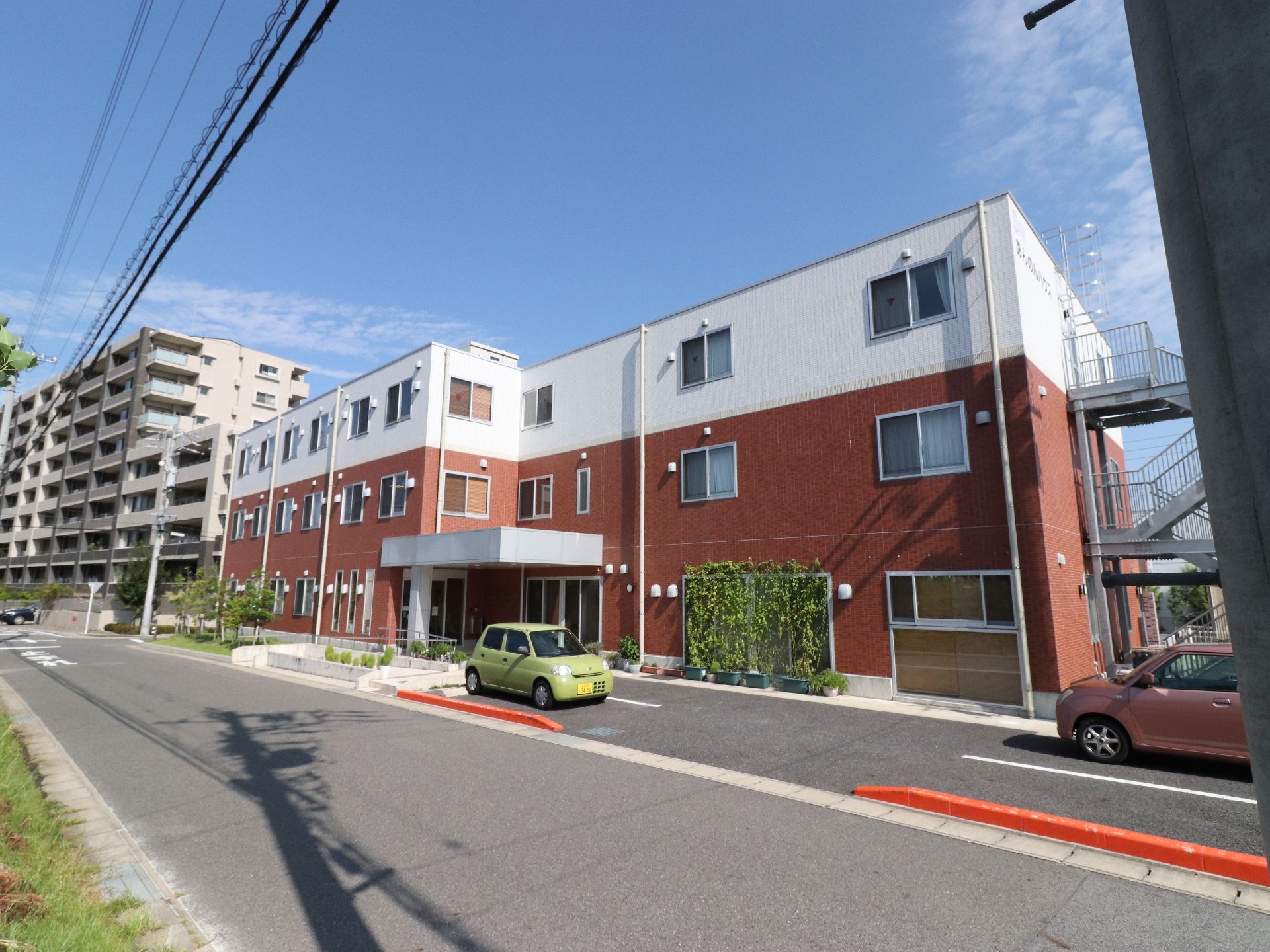 建物が正面にあり、そこの右側には外階段が付けられている。手前には道路が通っている。右手前には電柱がある。