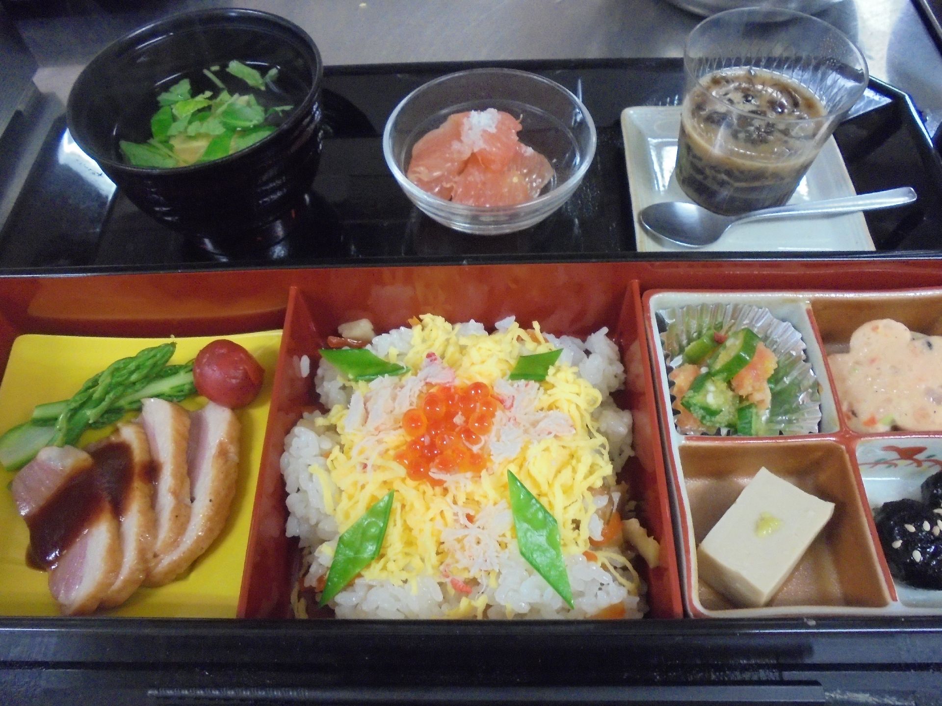 メインのおかずには茶色い肉と緑色の野菜が添えられている。ご飯はちらし寿司には黄色い錦糸卵とオレンジ色のイクラが乗っている。