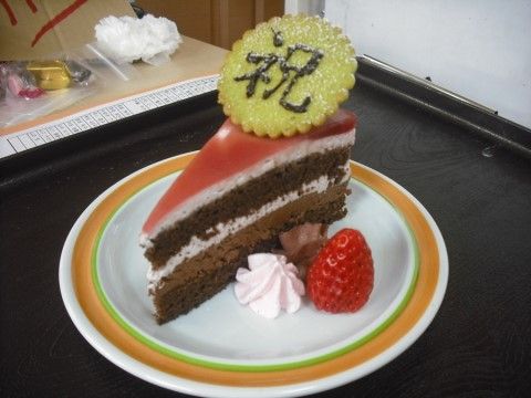 三角に切られたチョコレートケーキの上に、祝と書かれたクッキーがのっている一皿