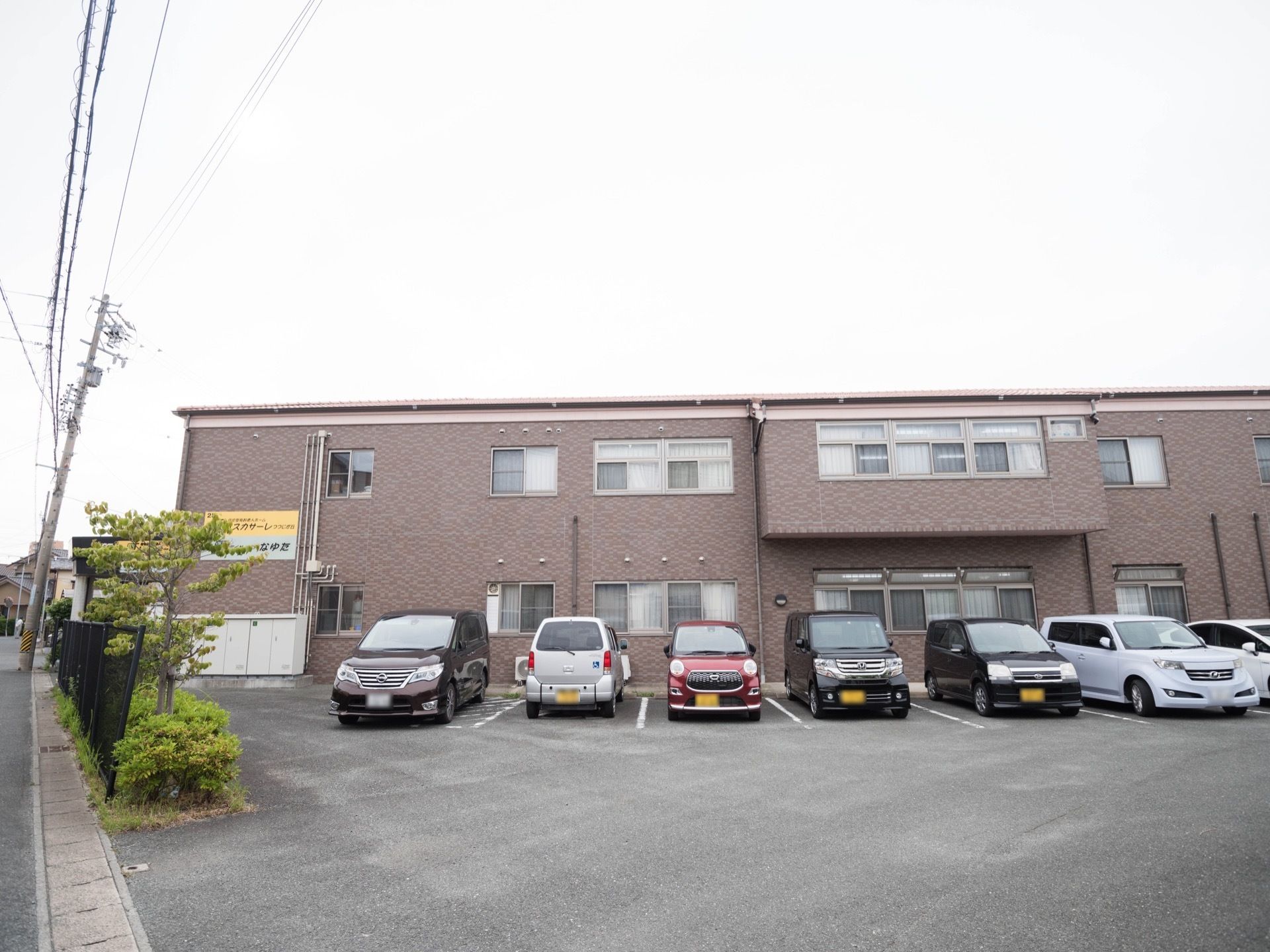 チャコールグレーの四角い二階建ての施設。外壁に施設名の看板が設置されている。駐車スペースが広く、多くの車を駐車することができる。