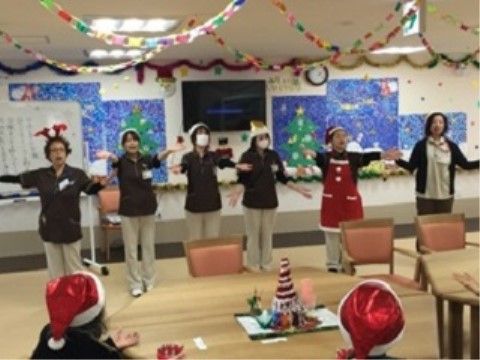 クリスマスの帽子をかぶった入居者の前で、パフォーマンスをしているスタッフたち